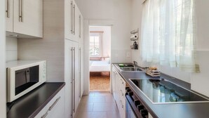 A modern kitchen with a microwave, stove, and sink. There is a window with sheer curtains and a view of the outside.