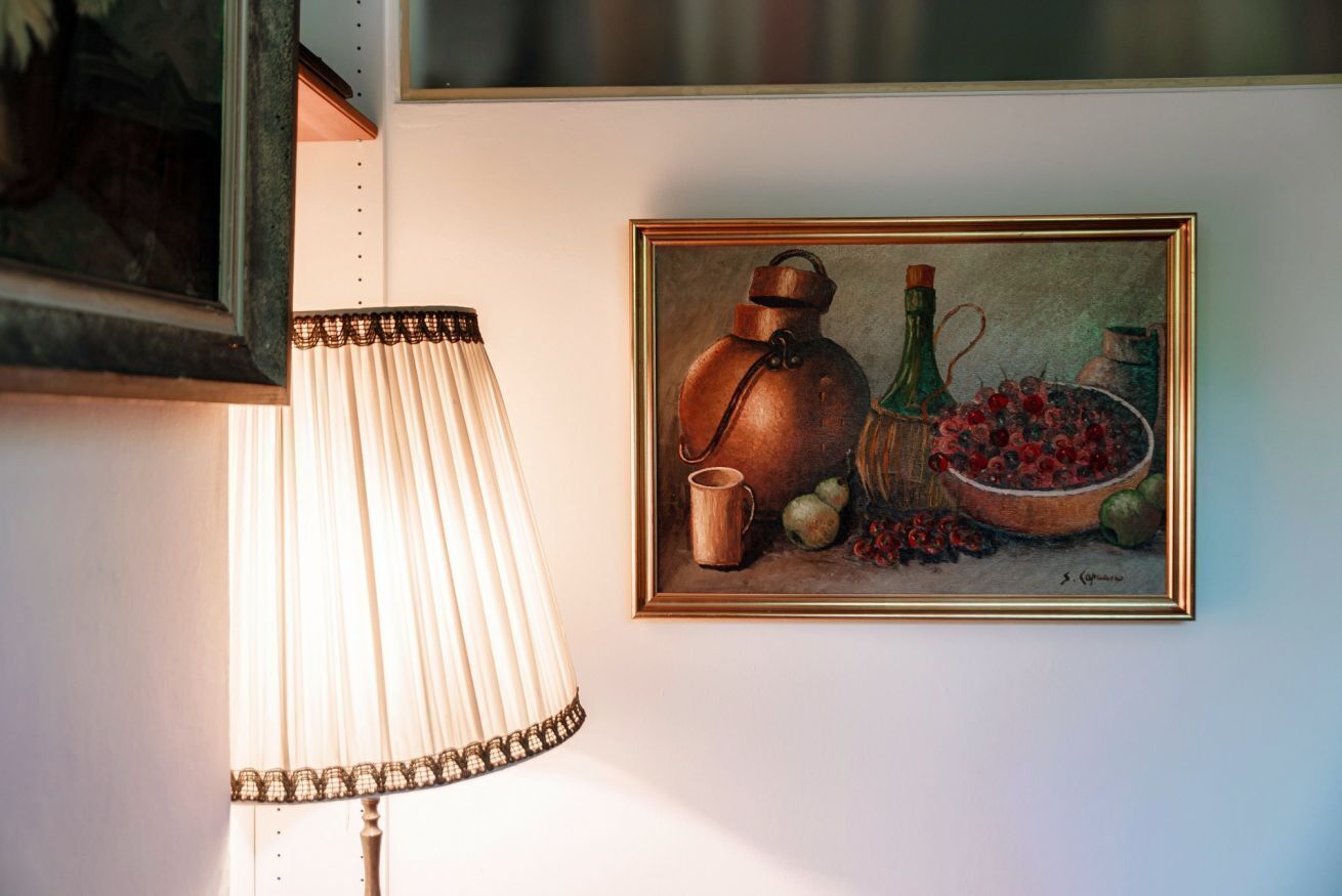 A lamp with a fringed shade and a framed still life painting on the wall.