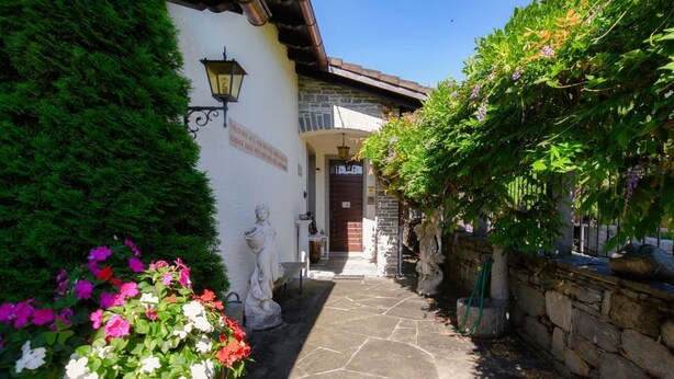 A stone pathway leading to a building with a red door, surrounded by lush greenery and flowering plants.