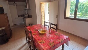 A dining area with a red tablecloth, wooden chairs, and a window with a view of greenery.
