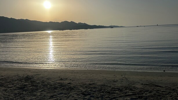 A beach with a clear sky, calm sea, and distant mountains.