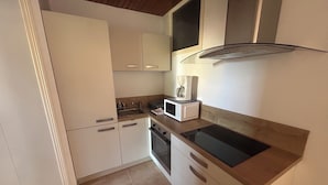 A compact kitchen with white cabinets, a microwave, a coffee maker, and a black induction cooktop.