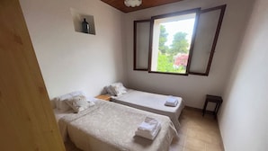 A small, clean room with two beds, a window, and a wooden ceiling.