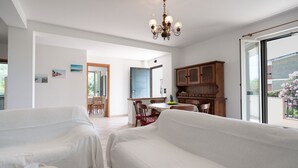 A living room with two white sofas, a dining table with chairs, a wooden cabinet, and a chandelier. - Villa Minerva Sperlongaresort (Sperlonga)