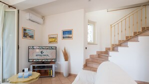 A spacious living area with a flat-screen TV, a staircase, and a large window. - Villa Minerva Sperlongaresort (Sperlonga)