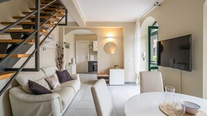 Ein modernes Wohnzimmer mit einer Couch, einem Esstisch, einem Fernseher und einer Treppe.