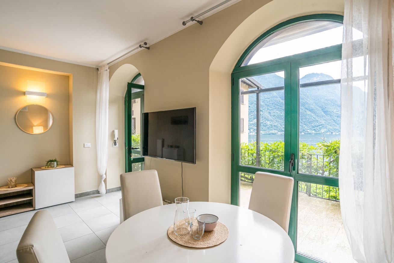 Una habitación moderna con una mesa redonda, sillas, un televisor y un balcón con vistas a la montaña.