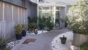 Un bâtiment moderne doté d’une entrée en verre, de plantes en pot et d’un chemin en béton.