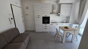 Une cuisine compacte dotée d’un four encastré, d’une table à manger avec des chaises, d’un canapé et d’un lave-linge.