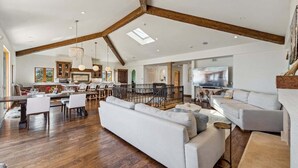 A spacious living area with a high ceiling, wooden beams, a large sofa, dining table, and chairs.