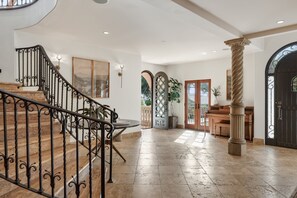 A grand staircase with ornate railings, a reception area with a desk and chairs, and a large column. - Italian Oceanview Estate | The Chosen Collection (Santa Barbara)