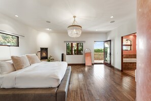 Ein geräumiges Schlafzimmer mit einem großen Bett, einer Chandelüster, einem Kamin und Blick ins Freie.