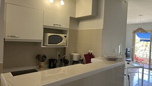 A modern kitchen with white cabinetry, a microwave, a coffee maker, and a small dining area with a table and chairs. - 3-Room Apartment Air-Conditioned, Sea View, Downtown Le Lavandou (Le Lavandou)