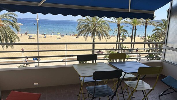 A balcony with a view of a beach, tables, chairs, and a railing. - 3-Room Apartment Air-Conditioned, Sea View, Downtown Le Lavandou (Le Lavandou)