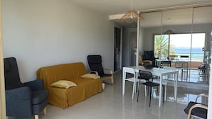 A modern living room with a sofa, chairs, a dining table, and a view of the sea through large windows. - 3-Room Apartment Air-Conditioned, Sea View, Downtown Le Lavandou (Le Lavandou)