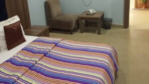 Habitación de hotel con cama, televisor montado en la pared, una mesita, una silla y una planta en maceta.