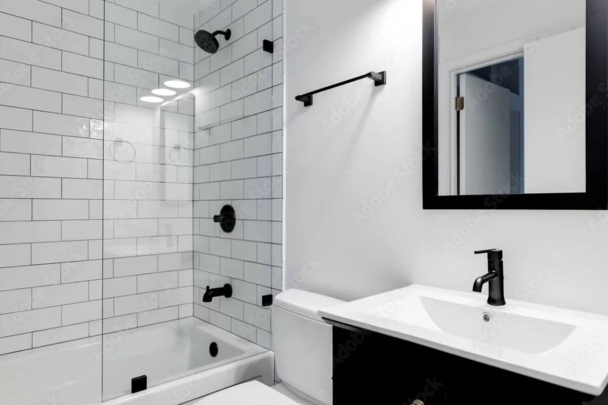 A modern bathroom with white tiled walls, a bathtub, a sink with a black faucet, and a mirror with a black frame.