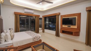 Une chambre d’hôtel avec un lit, un téléviseur fixé au mur, un ventilateur de plafond et de grandes fenêtres.