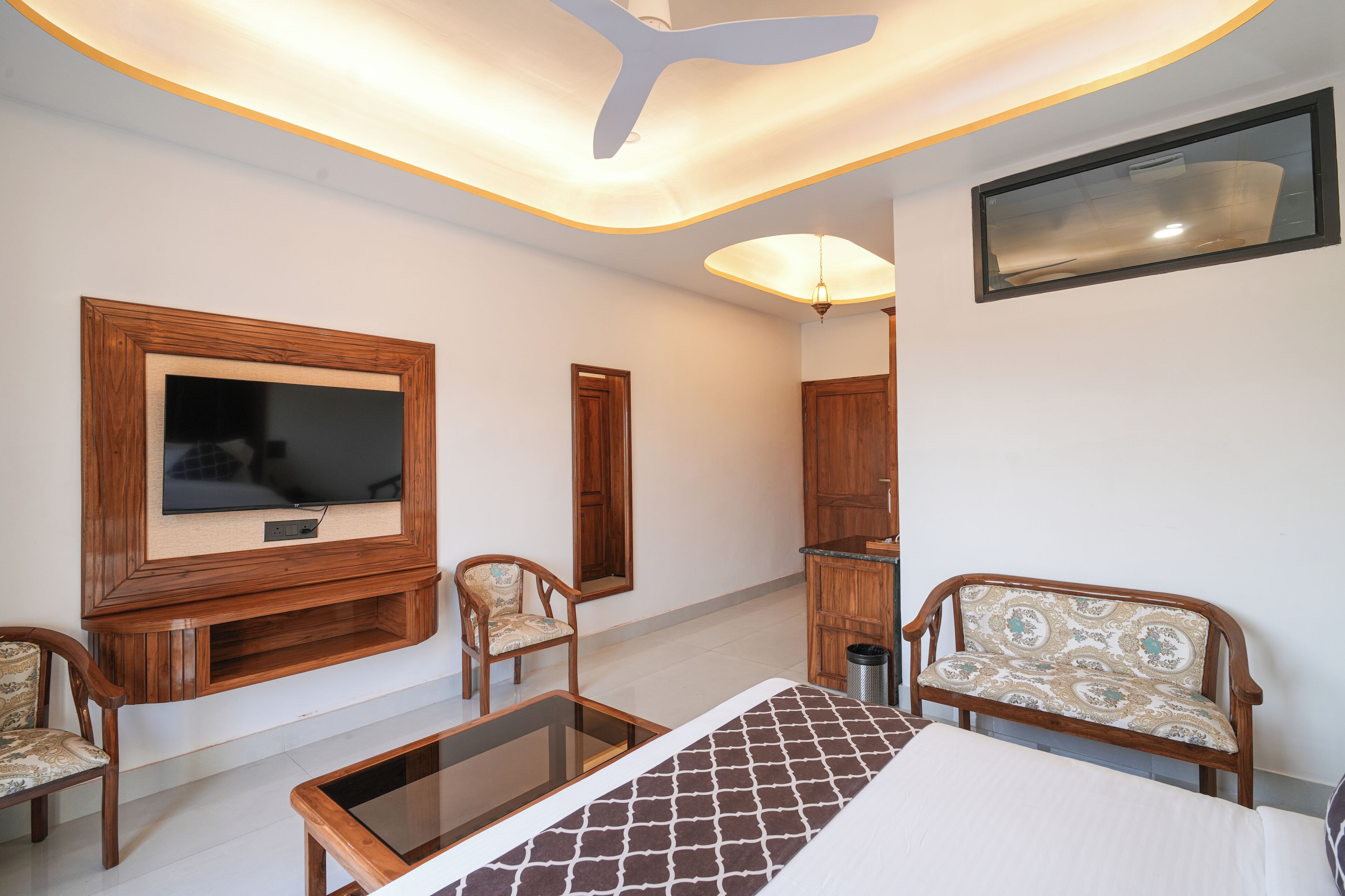 A room with a TV, wooden furniture, a ceiling fan, and a bed.