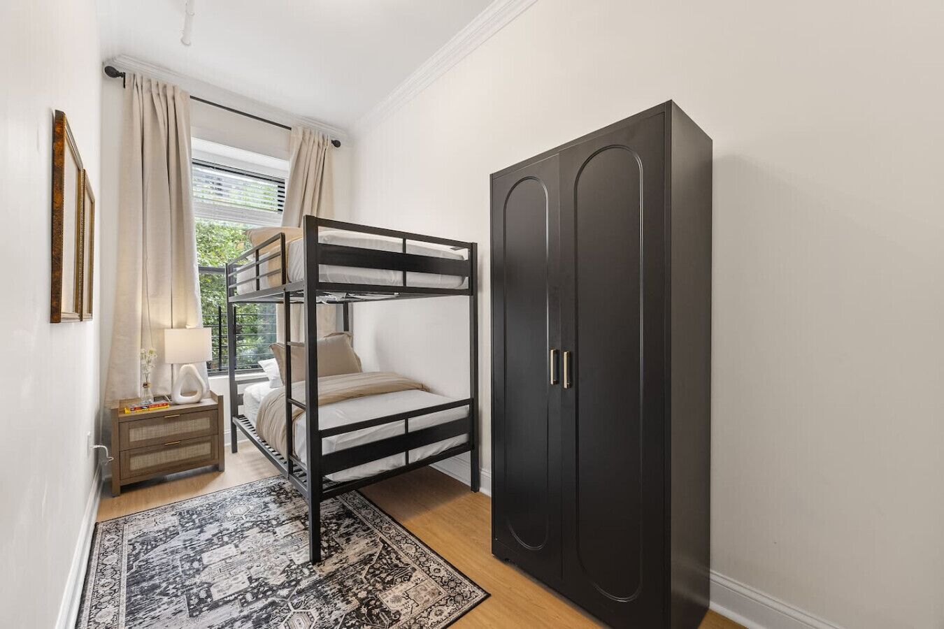 Ein kleines Schlafzimmer mit Etagenbett, Kleiderschrank, Nachttisch mit Lampe und einem gemusterten Teppich.