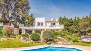 A two-story house with a pool, surrounded by a well-maintained garden and a white fence. - Luxury 5-Bedroom Villa Gardens Heated Pool, Jacuzzi & Sea Views – Estepona (Bahía Dorada)