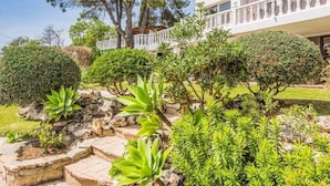 A well-maintained garden with various shrubs and a stone pathway leading to a building with a white facade and balconies. - Luxury 5-Bedroom Villa Gardens Heated Pool, Jacuzzi & Sea Views – Estepona (Bahía Dorada)