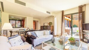 A modern living room with a sofa, armchairs, a glass coffee table, and a television.