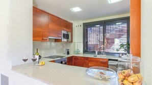 A modern kitchen with wooden cabinets, a microwave, and a window with blinds.