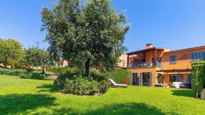 A two-story house with a large tree in the front yard, a pool, and a well-maintained lawn.