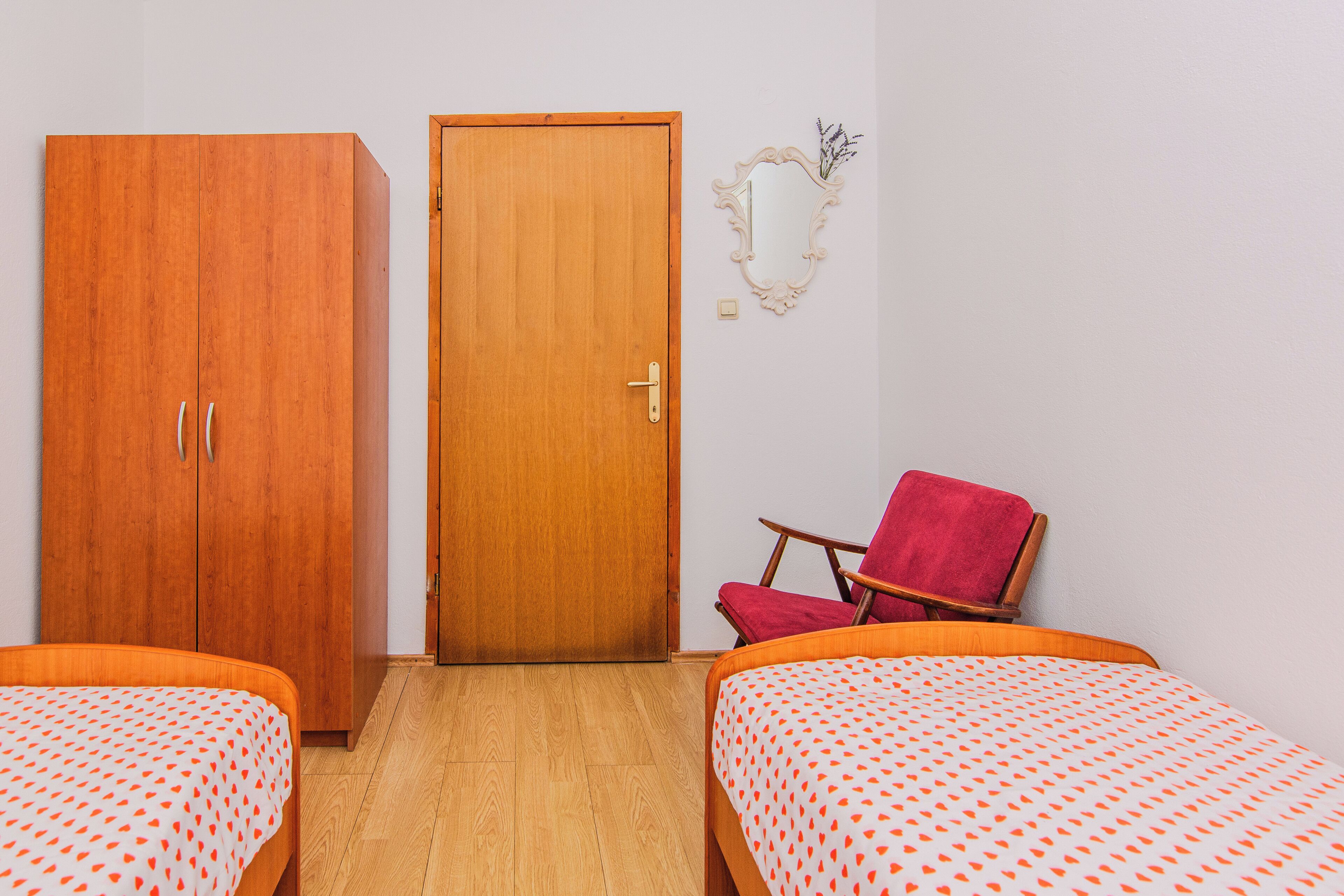 Een kamer met twee bedden, een kledingkast, een deur, een stoel en een spiegel aan de muur.