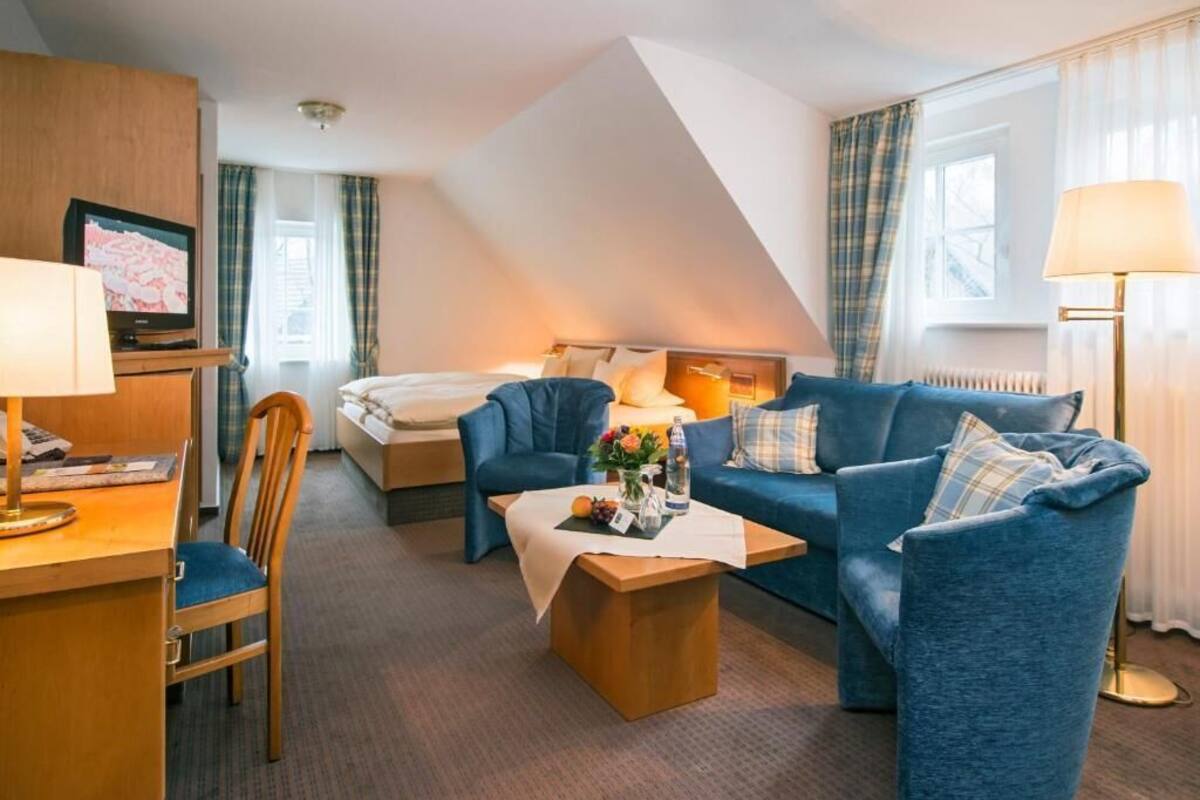 Una habitación de hotel con una cama, un sofá azul, un escritorio de madera, una silla y una lámpara.