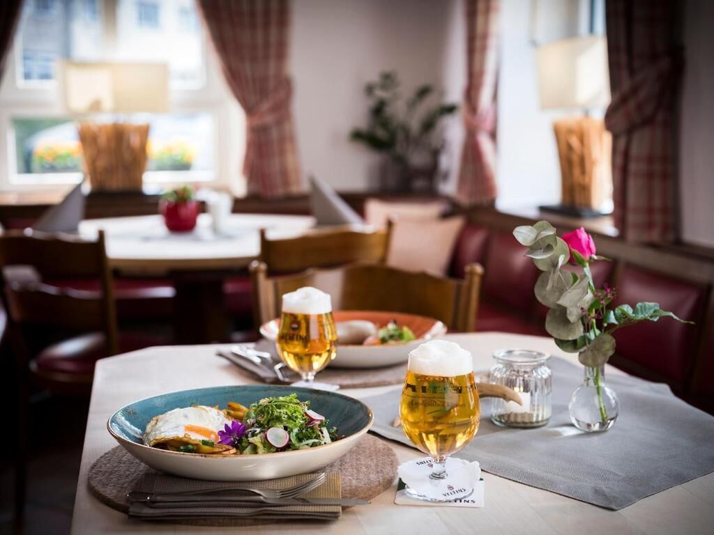 Een eettafel met een bord eten, twee bierglazen en een vaas met bloemen.