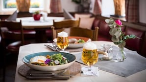 Ein Esstisch mit einem Teller Essen, zwei Biergläsern und einer Blumenvase.