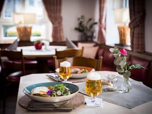 A dining table with a plate of food, two beer glasses, and a vase with flowers. - Landgasthof Kleiner  (Sundern)