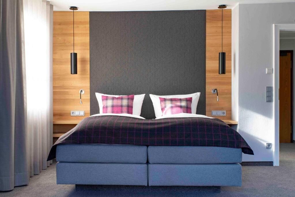 Een moderne slaapkamer met een bed, twee nachtkastjes, een houten accentmuur en een grijs hoofdeinde.