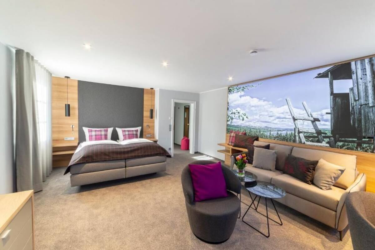 Un dormitorio moderno con cama, sofá, sillón y un gran ventanal con vistas.