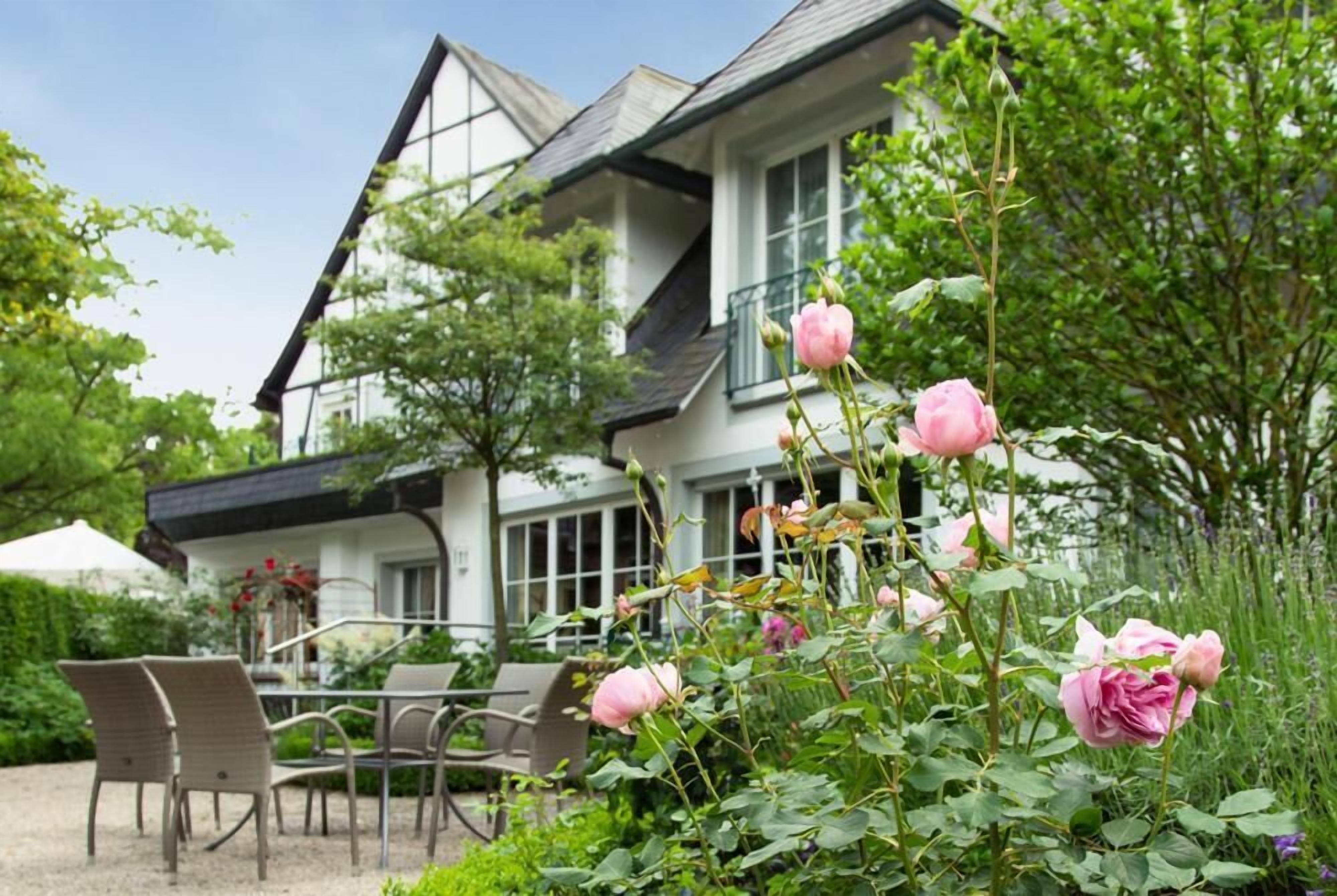 A house with a balcony, a garden with roses, and outdoor seating.