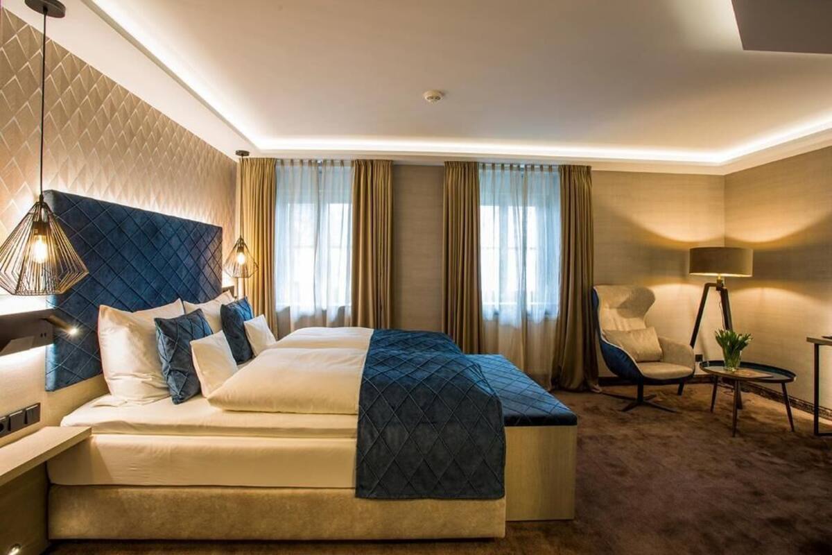 Una habitación de hotel con una cama, una silla, una lámpara y una mesita.