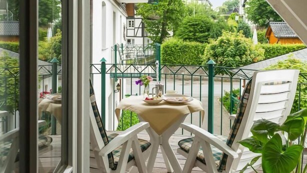 Ein Balkon mit Tisch und Stühlen, Blick auf einen Baum und ein Gebäude im Hintergrund.