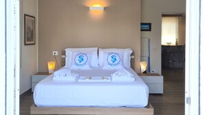 Una cama bien hecha con sábanas y almohadas blancas, una mesita de noche con lámpara, y una lámpara de pared.