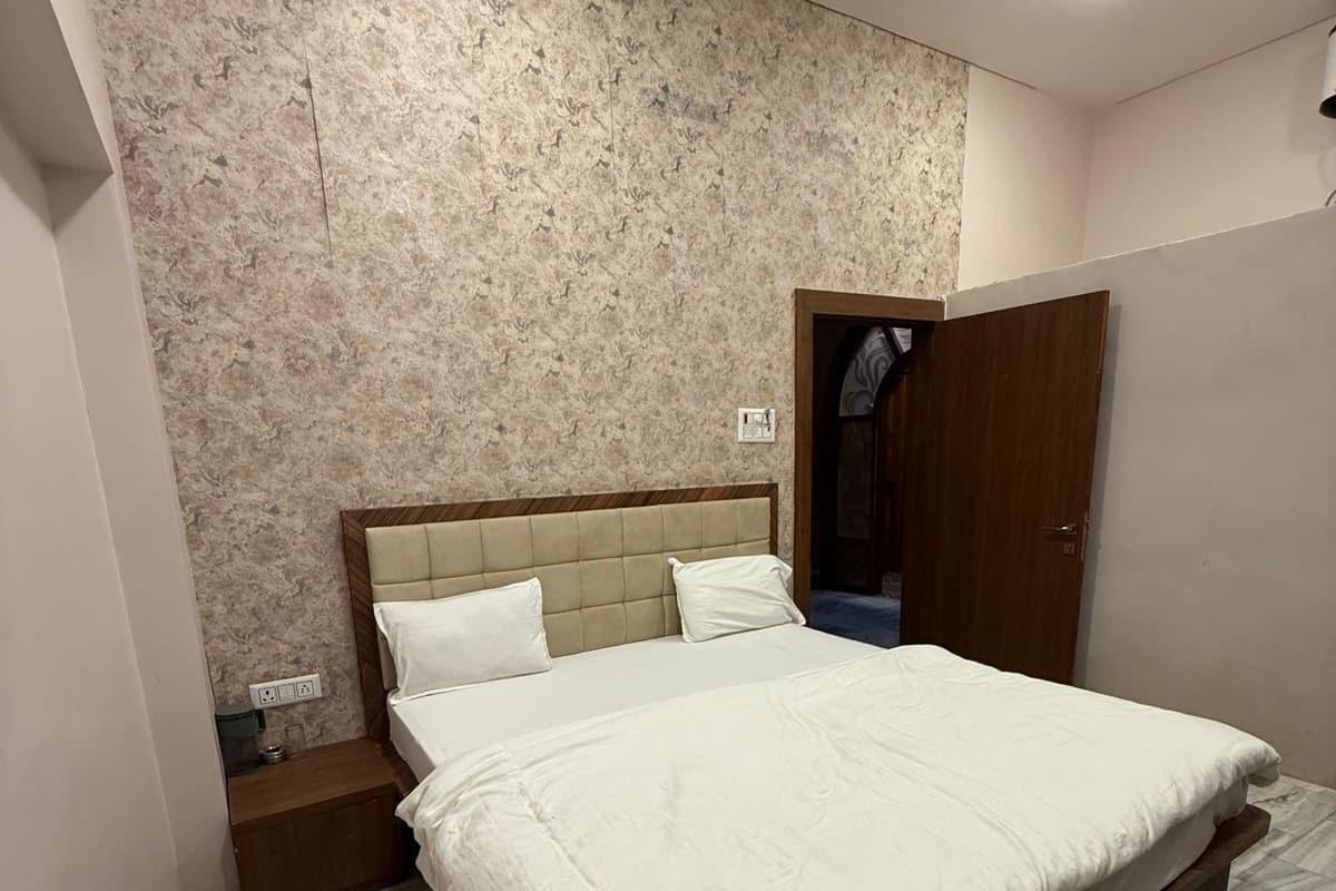 Un dormitorio con cama, cabecera de madera, pared con diseño de mármol, puerta de madera y suelo de baldosas.