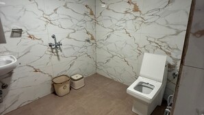 Een badkamer met marmeren wanden, een toilet, een wastafel en een douche.