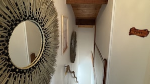A hallway with a wooden ceiling, a large mirror, and a staircase leading to another room.