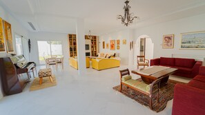 A spacious living room with a piano, a yellow sofa, a red sofa, and a dining table.