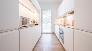 Ett smalt, modernt kök med vita skåp, en mikrovågsugn, en diskho och en spis.