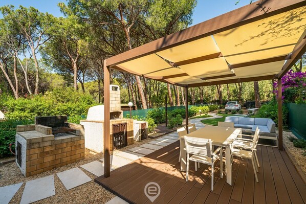 Un patio exterior con una parrilla, zona de estar y una pérgola que proporciona sombra.