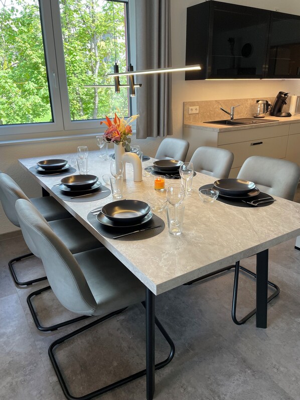Un comedor moderno con una mesa de mármol, platos negros y sillas grises.