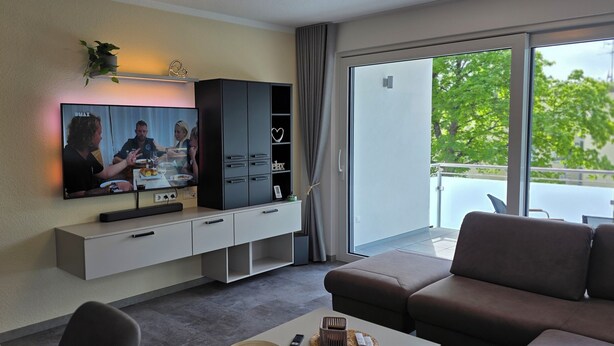 Una sala de estar moderna con una televisión de pantalla plana, un sofá, una mesa de centro y un ventanal corredero que da a un balcón.