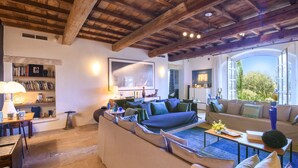 A spacious living room with a high wooden ceiling, a large sofa, a coffee table, and a bookshelf. - Mas Cicada (Paradou)