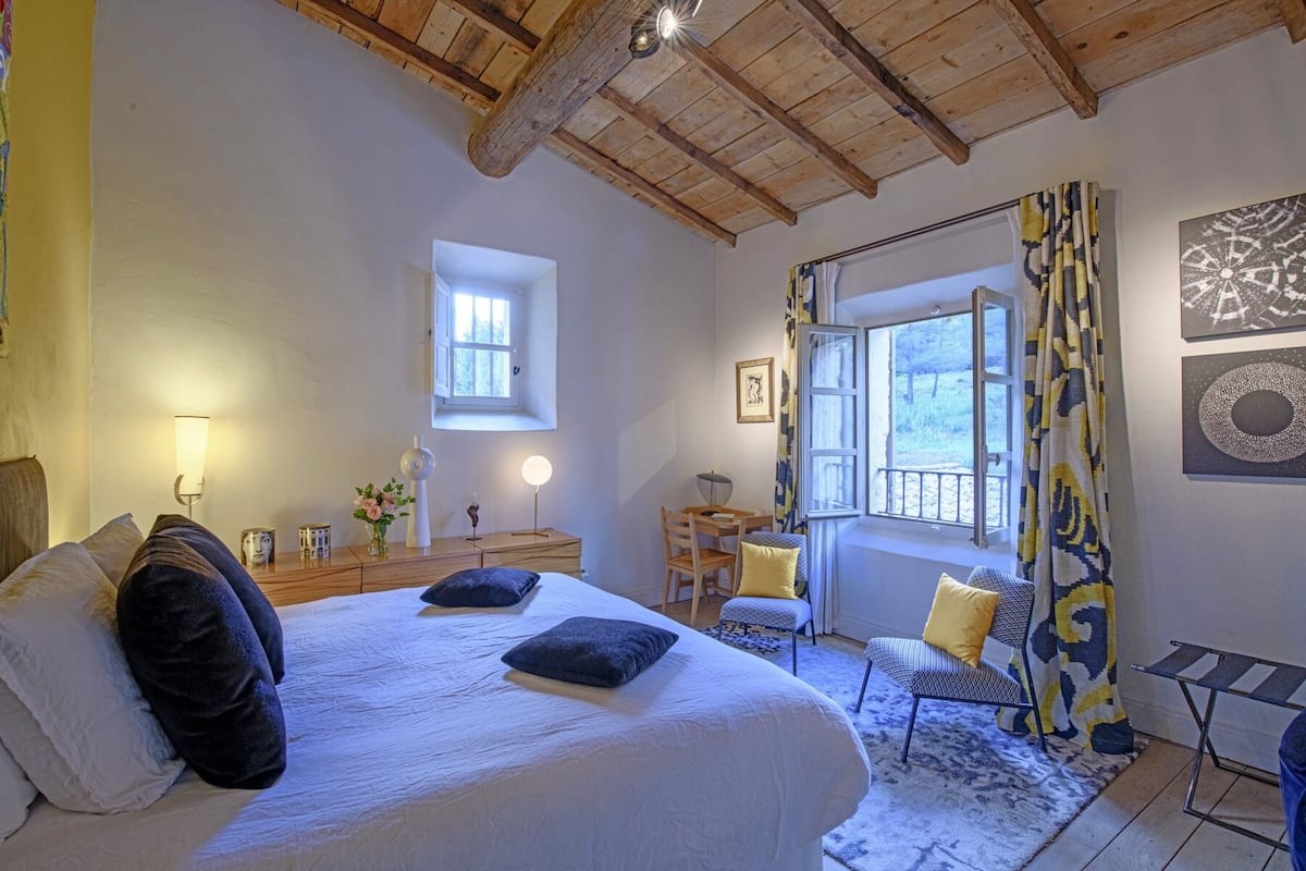 Une chambre à coucher avec un grand lit, un bureau, une chaise et une fenêtre avec des rideaux.